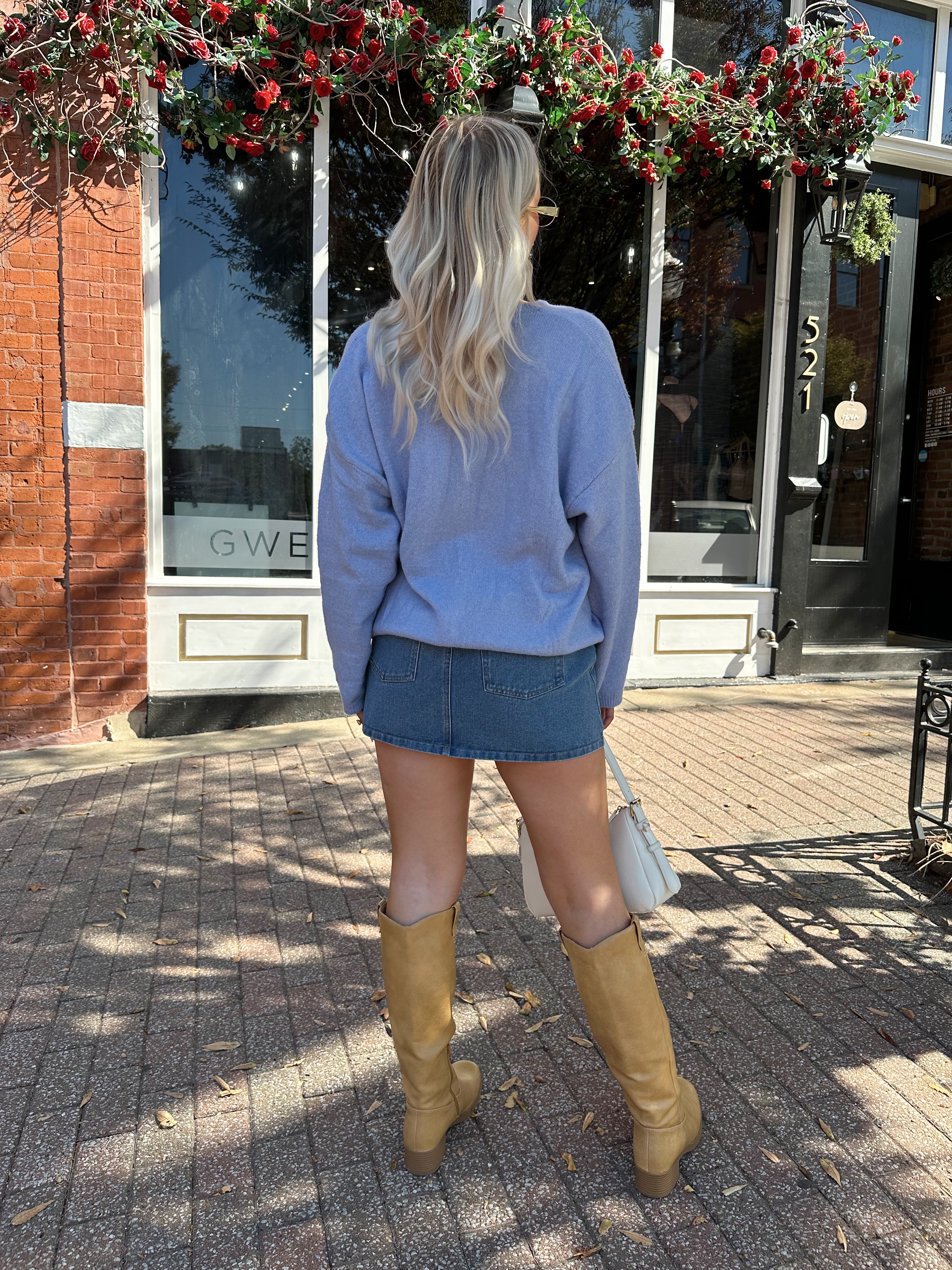 Woman wearing baby blue knit button down cardigan with denim skirt. 