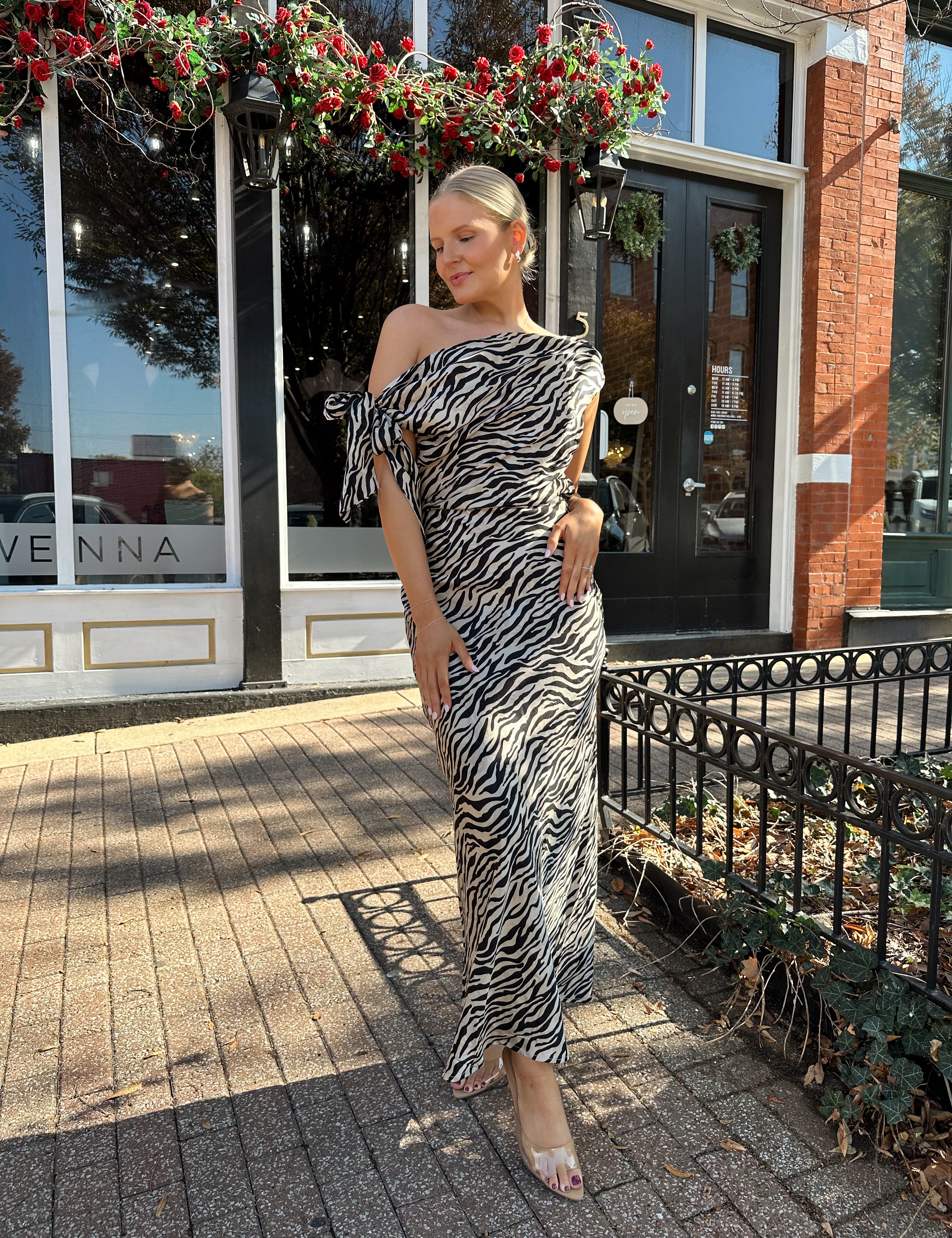 Woman wearing zebra print satin maxi dress with asymmetrical neckline. 