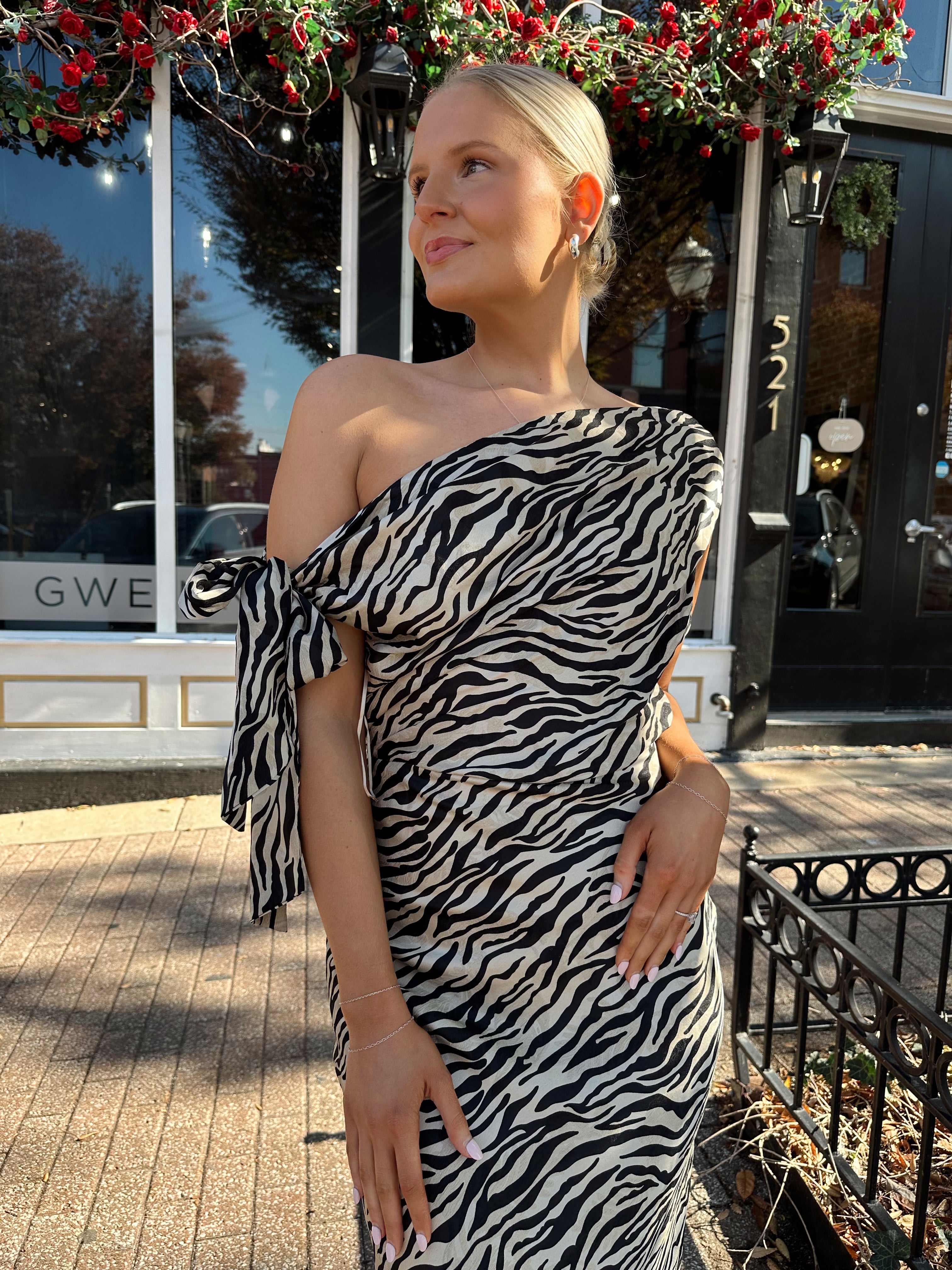 Woman wearing zebra print satin maxi dress with asymmetrical neckline. 