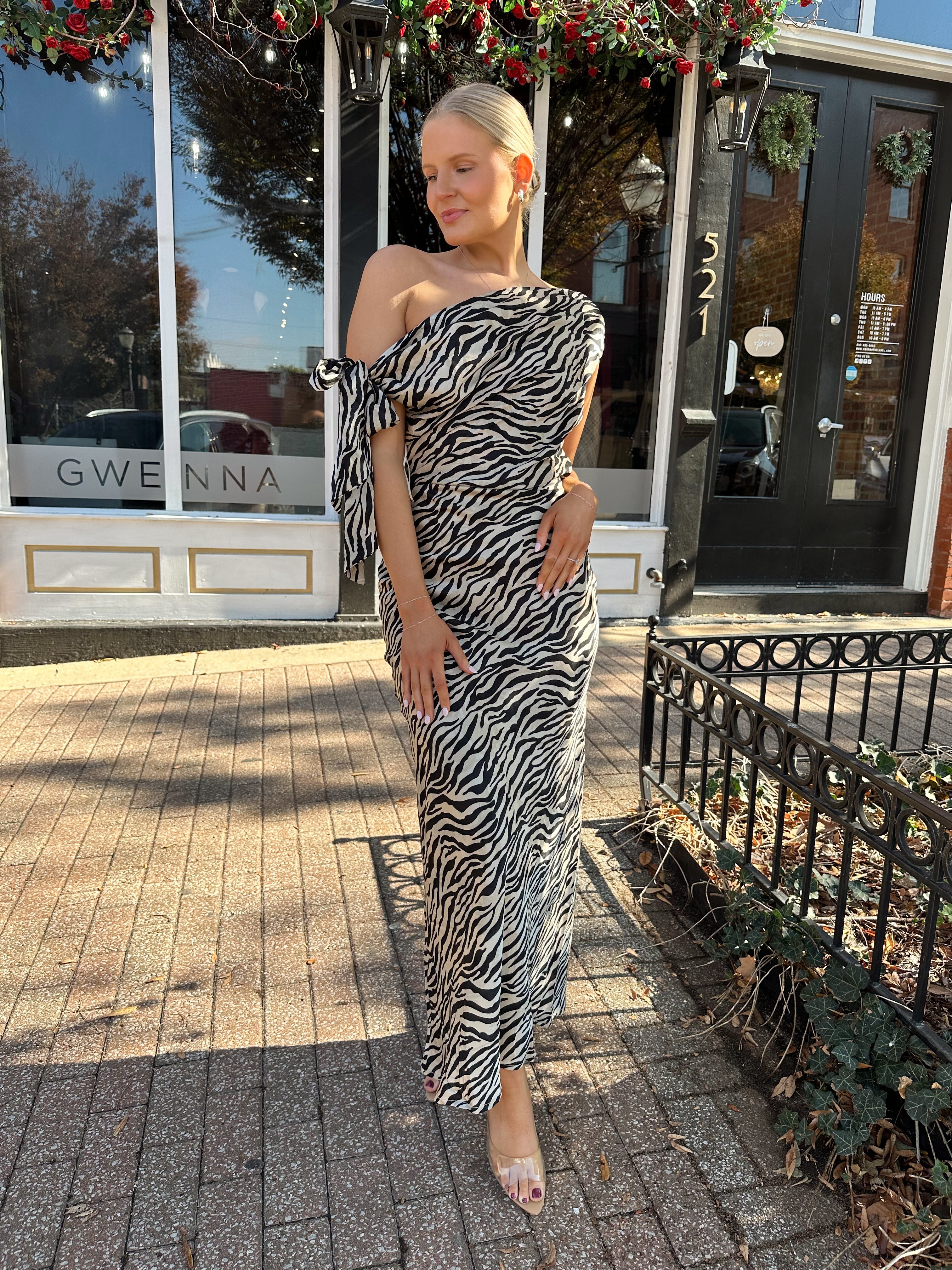 Woman wearing zebra print satin maxi dress with asymmetrical neckline. 