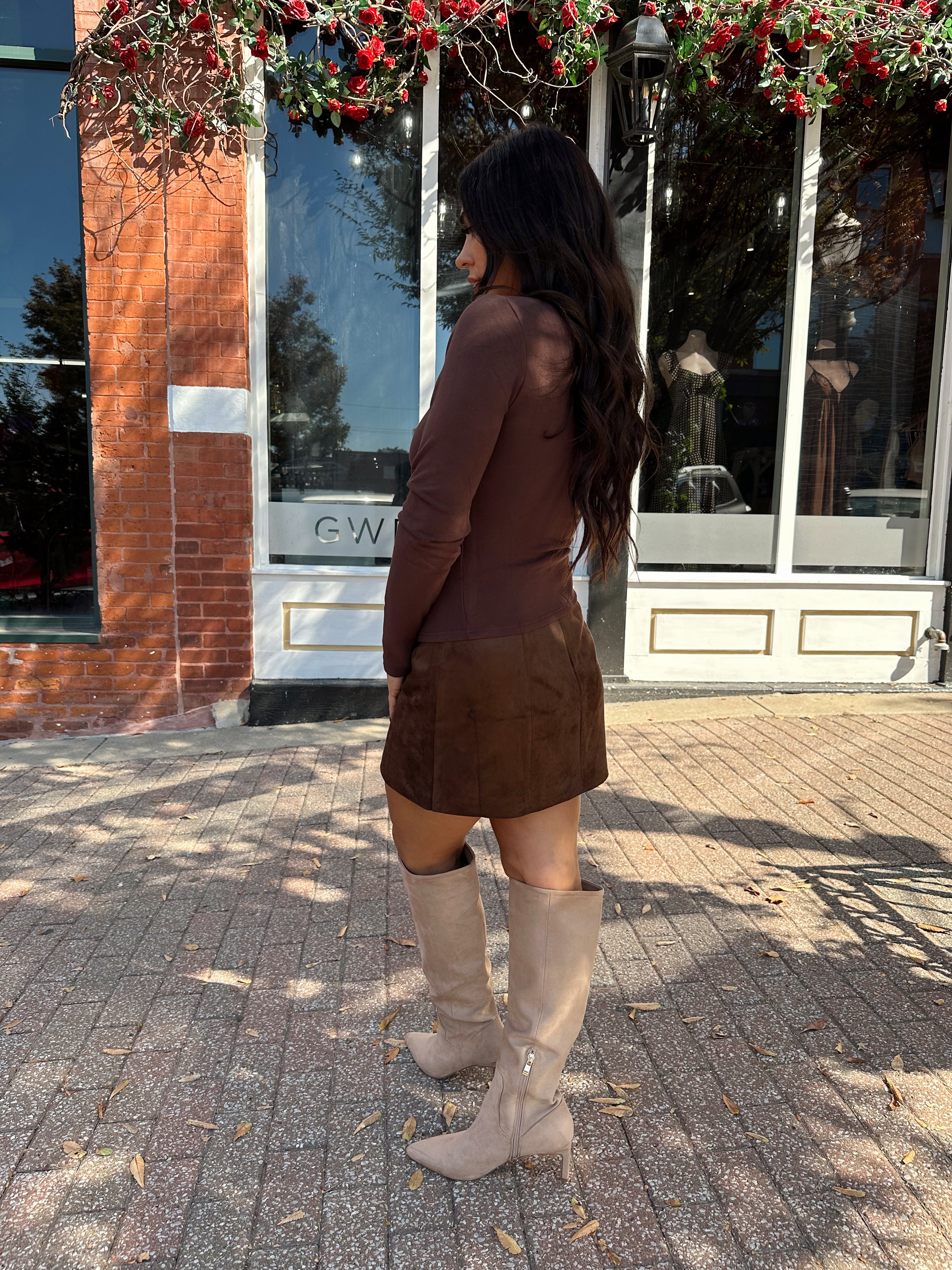 Woman wearing chocolate brown long sleeve top with gold detailing.
