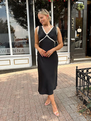 Woman wearing black satin fit to flare dress with white ruffle trim.