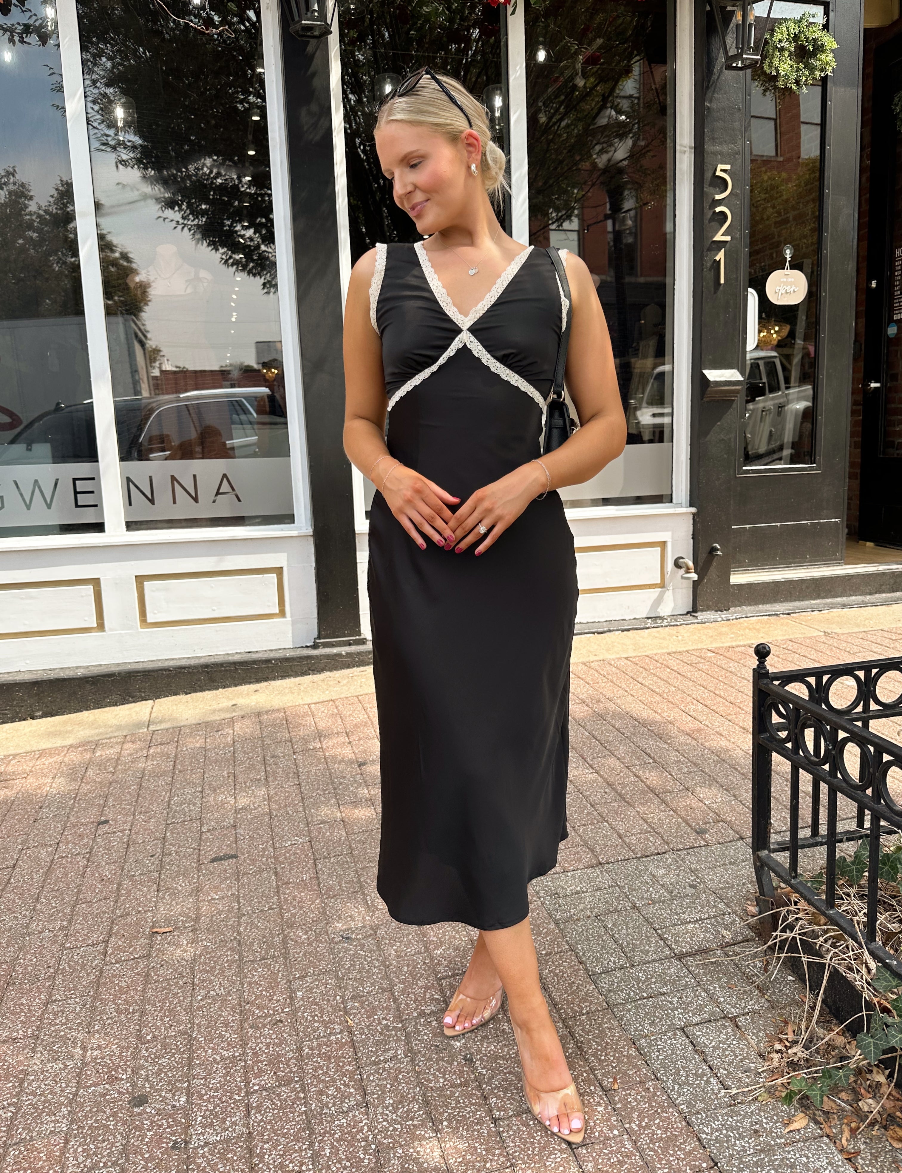 Woman wearing black satin fit to flare dress with white ruffle trim.