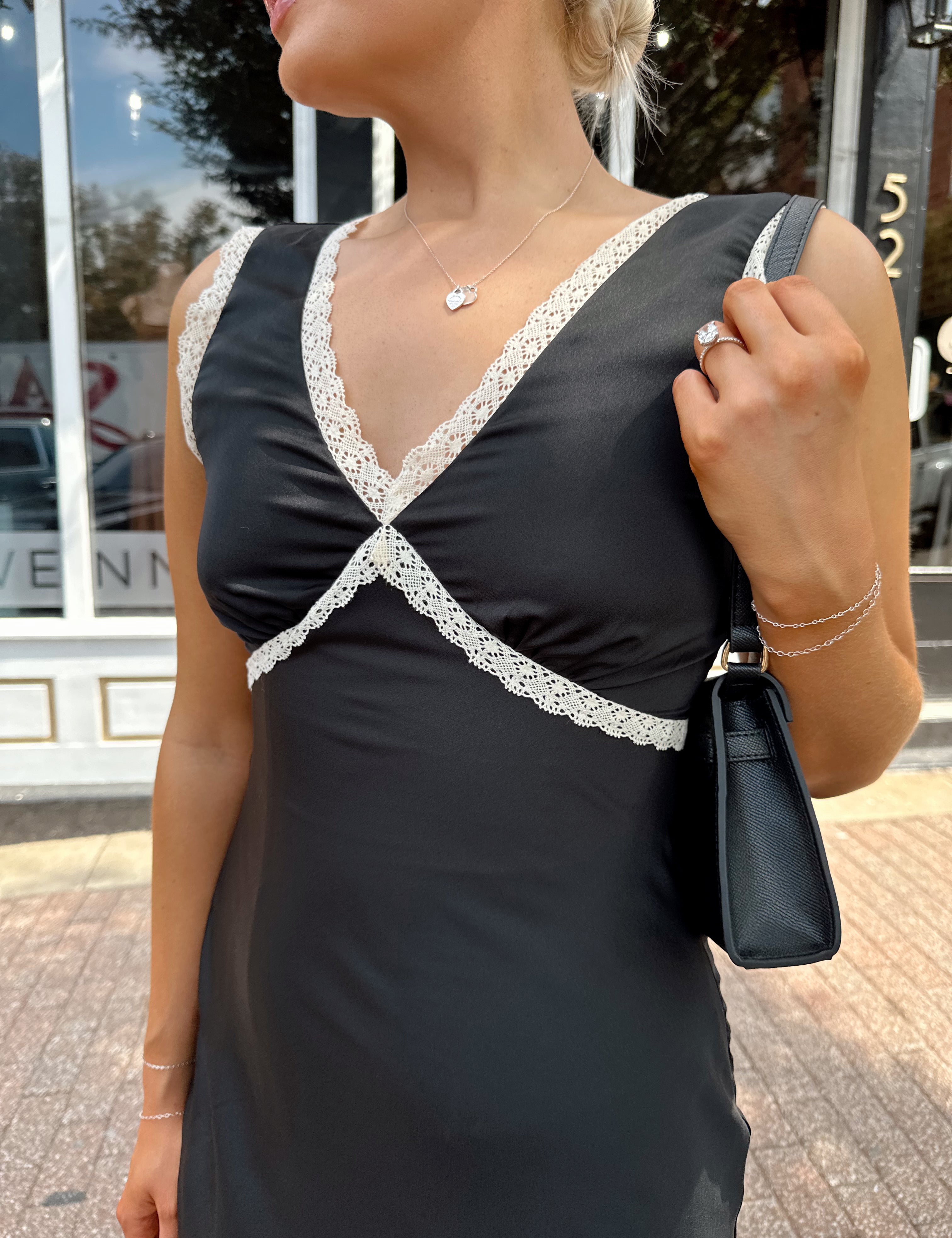 Woman wearing black satin fit to flare dress with white ruffle trim.
