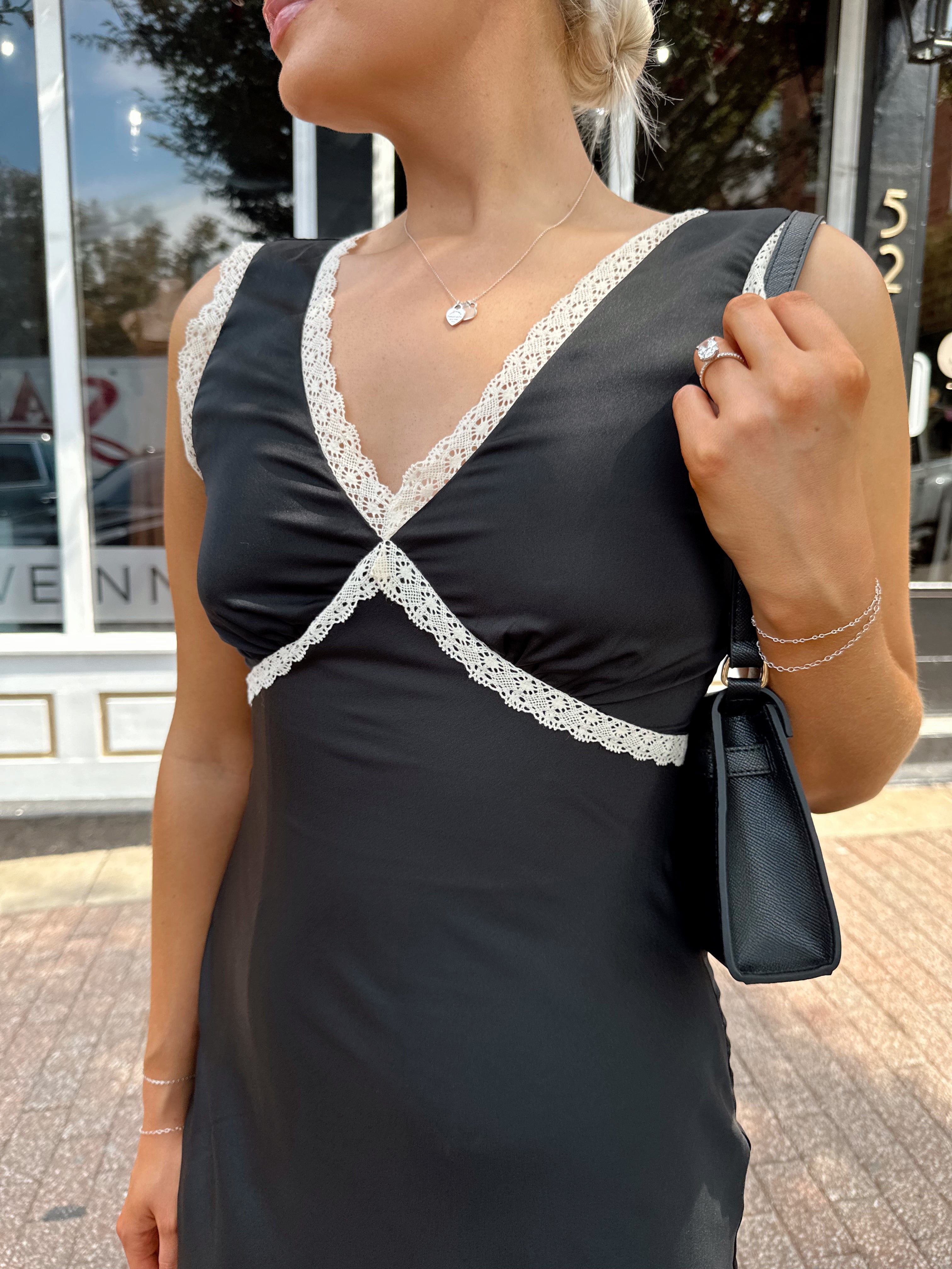 Woman wearing black satin fit to flare dress with white ruffle trim.