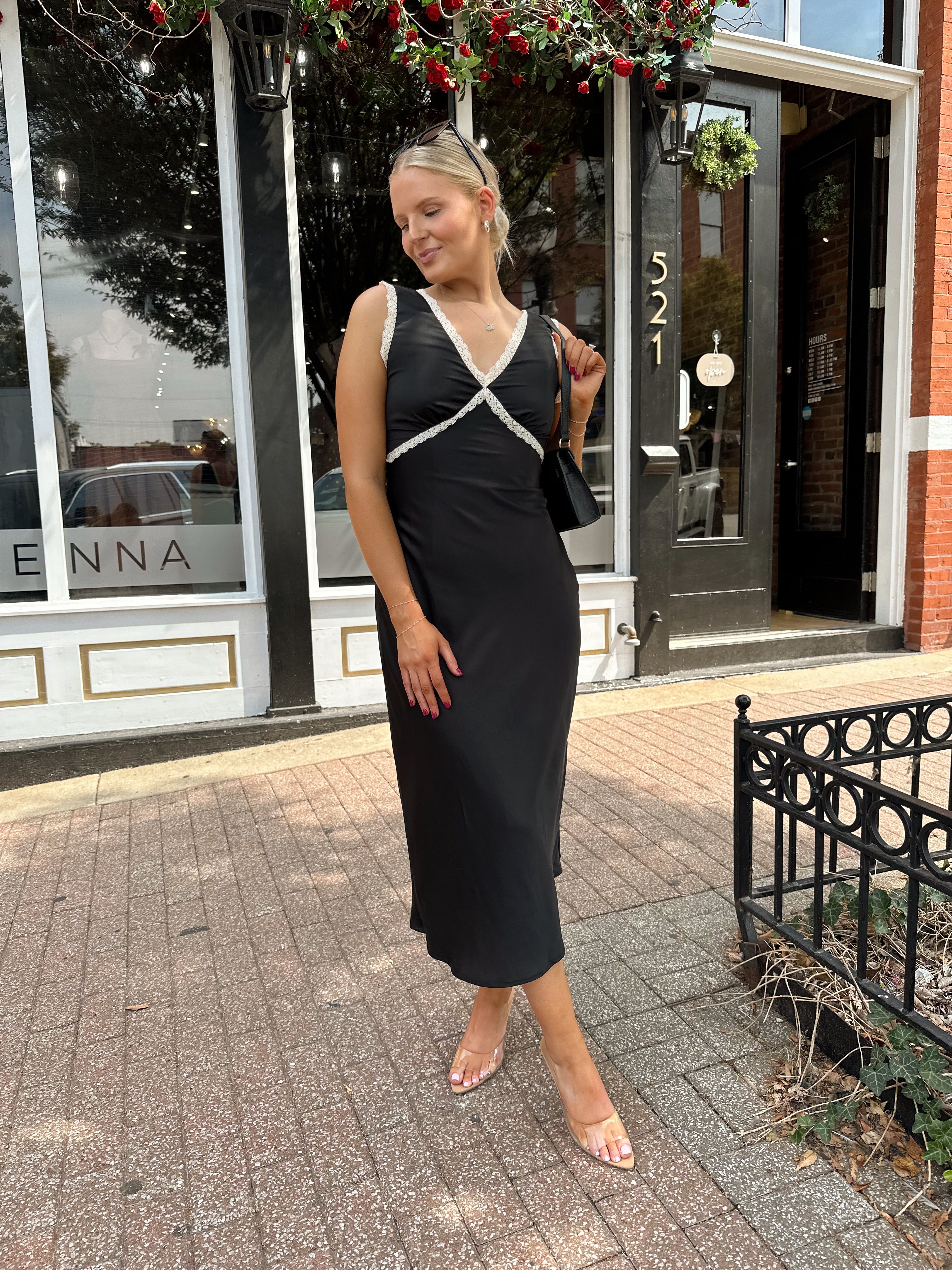 Woman wearing black satin fit to flare dress with white ruffle trim.