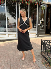 Woman wearing black satin fit to flare dress with white ruffle trim.