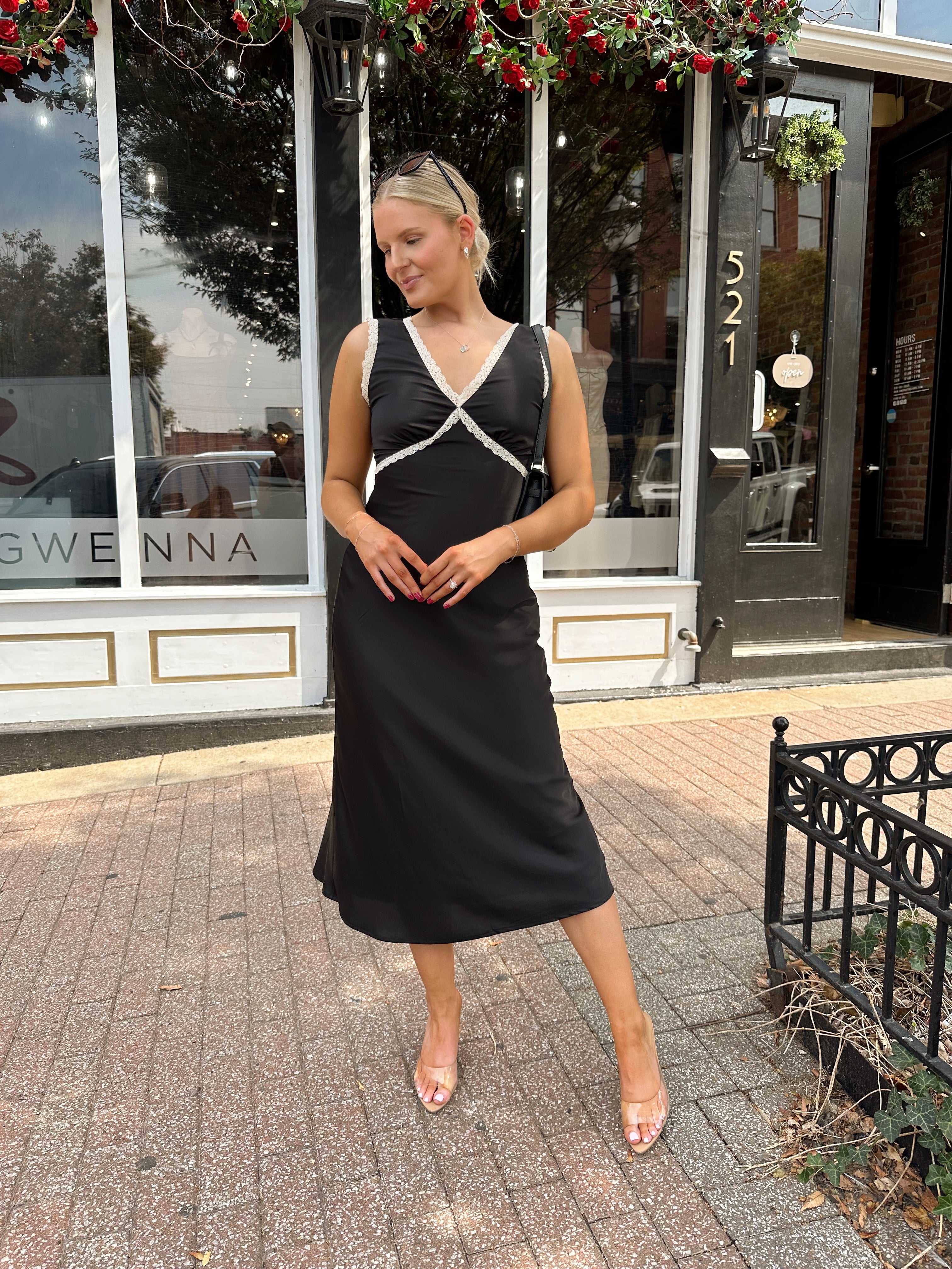 Woman wearing black satin fit to flare dress with white ruffle trim.