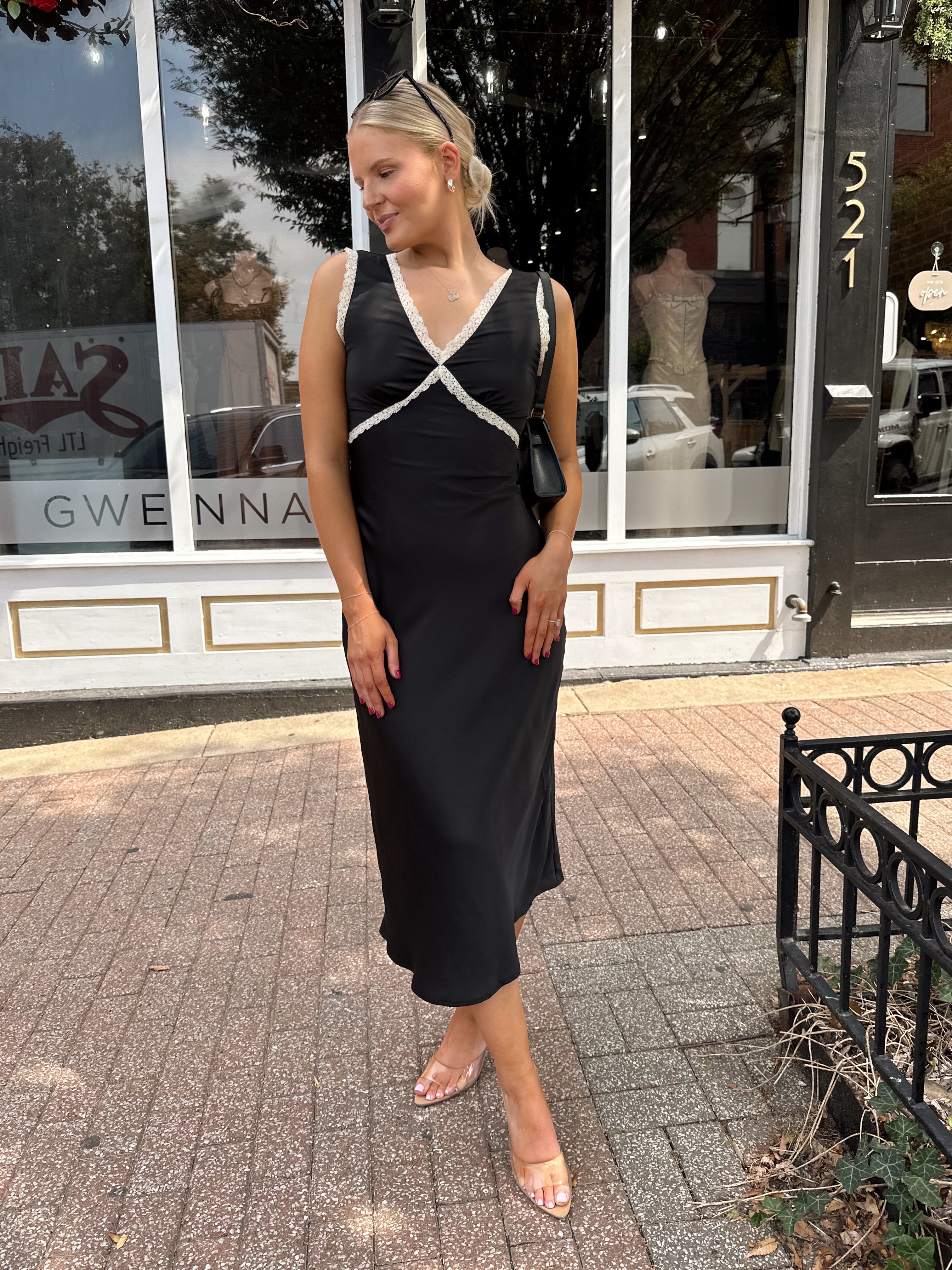 Woman wearing black satin fit to flare dress with white ruffle trim.