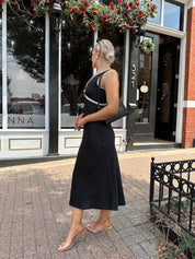 Woman wearing black satin fit to flare dress with white ruffle trim.