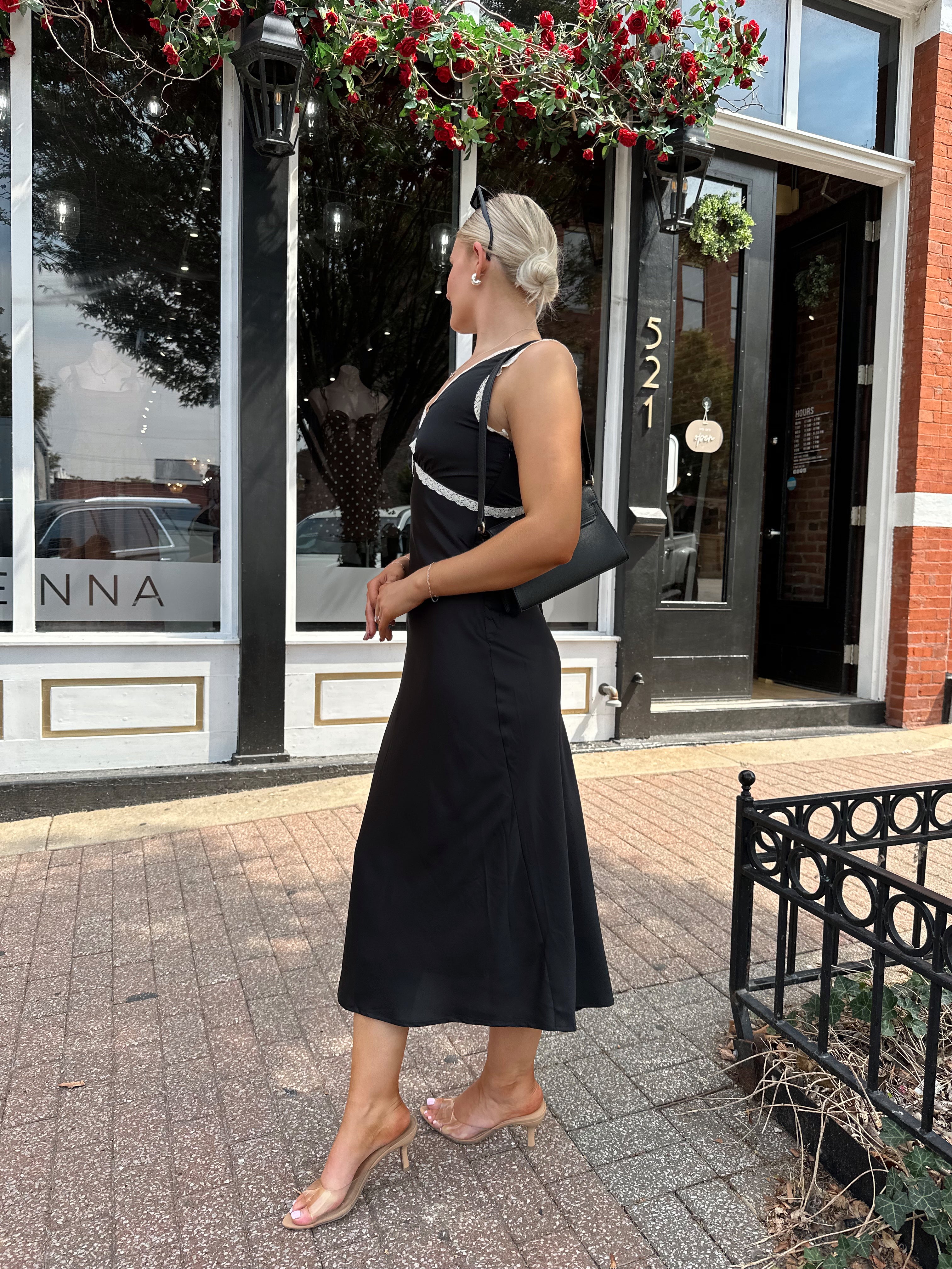 Woman wearing black satin fit to flare dress with white ruffle trim.