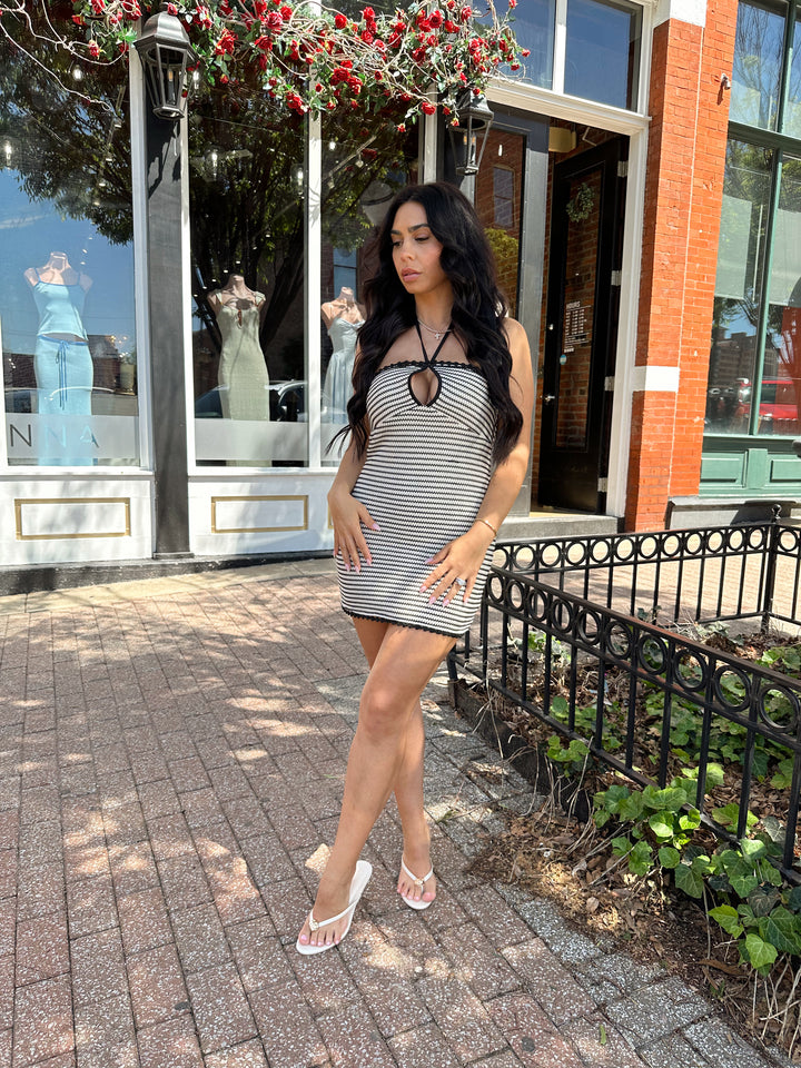 Woman wearing black and neutral striped crochet mini dress with a self tie halter neck.  