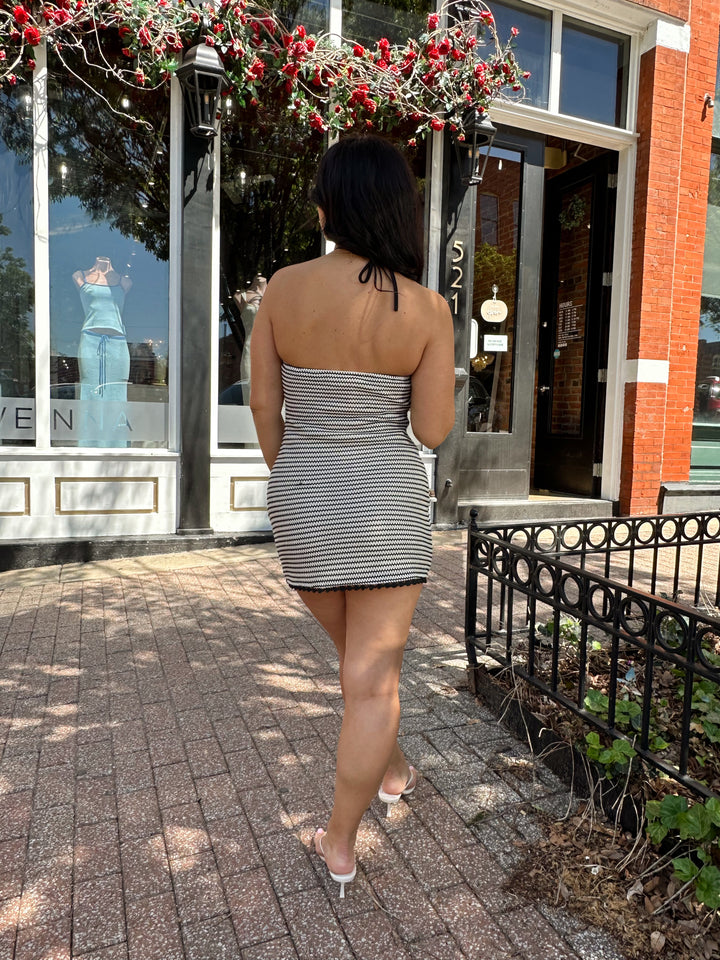 Woman wearing black and neutral striped crochet mini dress with a self tie halter neck.  
