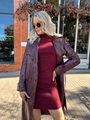 Woman wearing burgundy knit mock neck mini dress with leather trench coat.