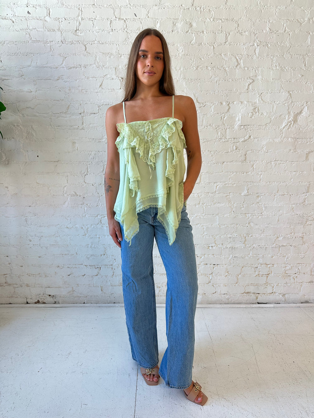 Woman wearing sage green flouncy tiered top with medium wash jeans. 
