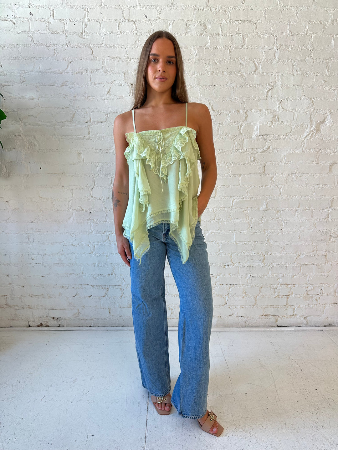Woman wearing sage green flouncy tiered top with medium wash jeans. 
