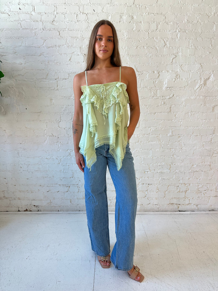 Woman wearing sage green flouncy tiered top with medium wash jeans. 