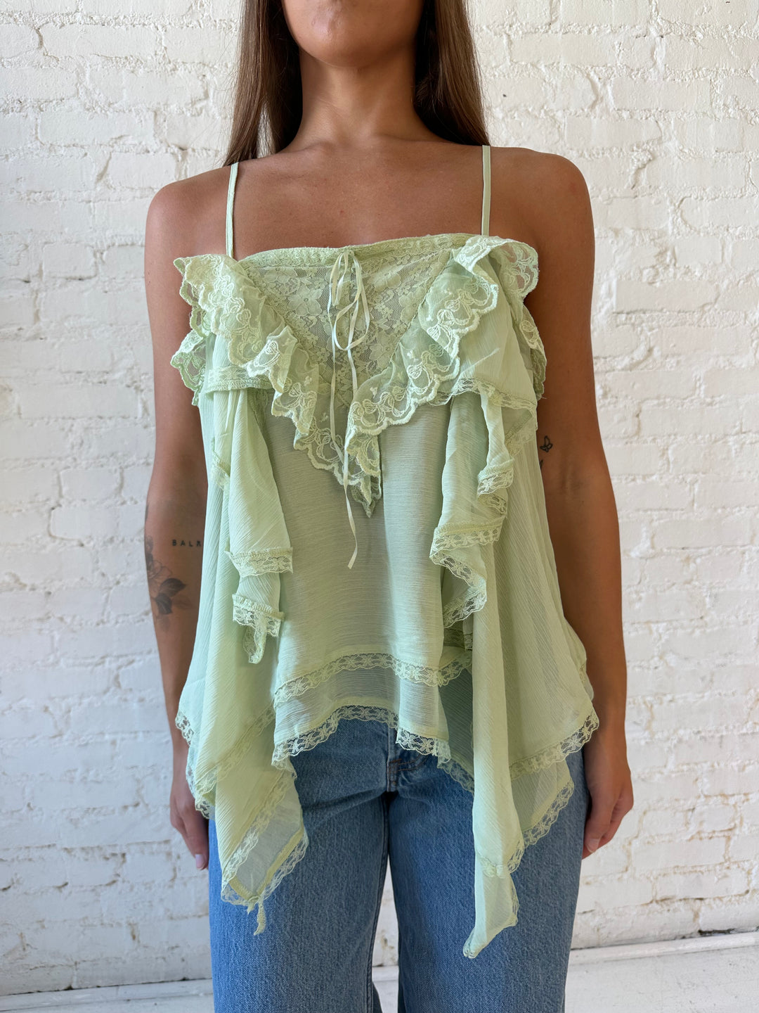 Woman wearing sage green flouncy tiered top with medium wash jeans. 