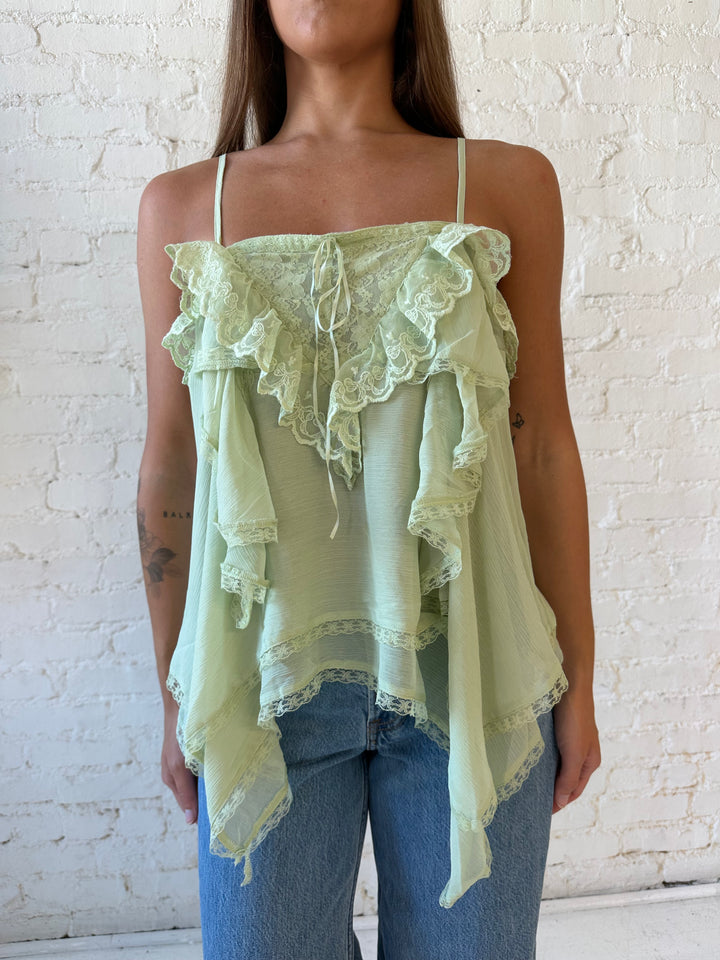 Woman wearing sage green flouncy tiered top with medium wash jeans. 