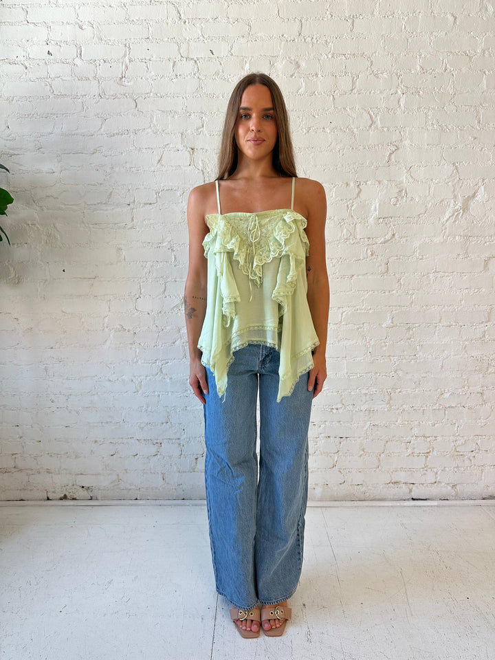 Woman wearing sage green flouncy tiered top with medium wash jeans. 