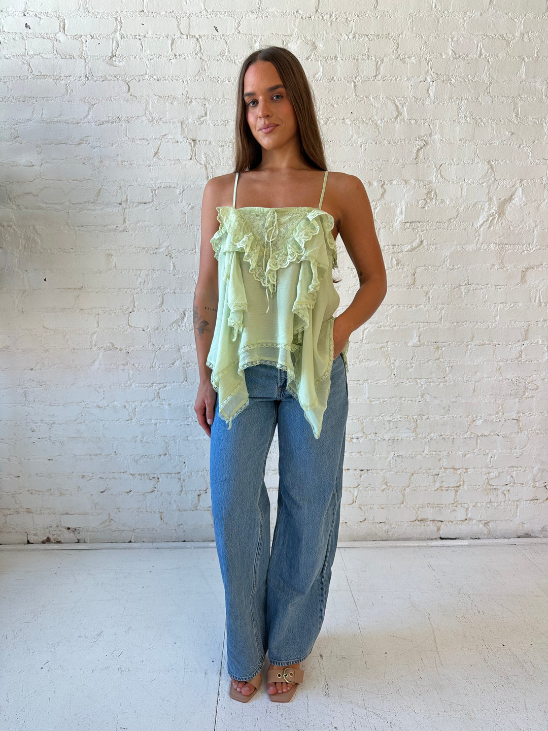 Woman wearing sage green flouncy tiered top with medium wash jeans. 