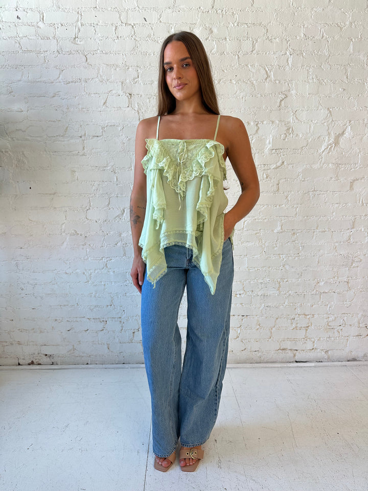Woman wearing sage green flouncy tiered top with medium wash jeans. 