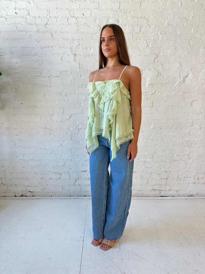 Woman wearing sage green flouncy tiered top with medium wash jeans. 