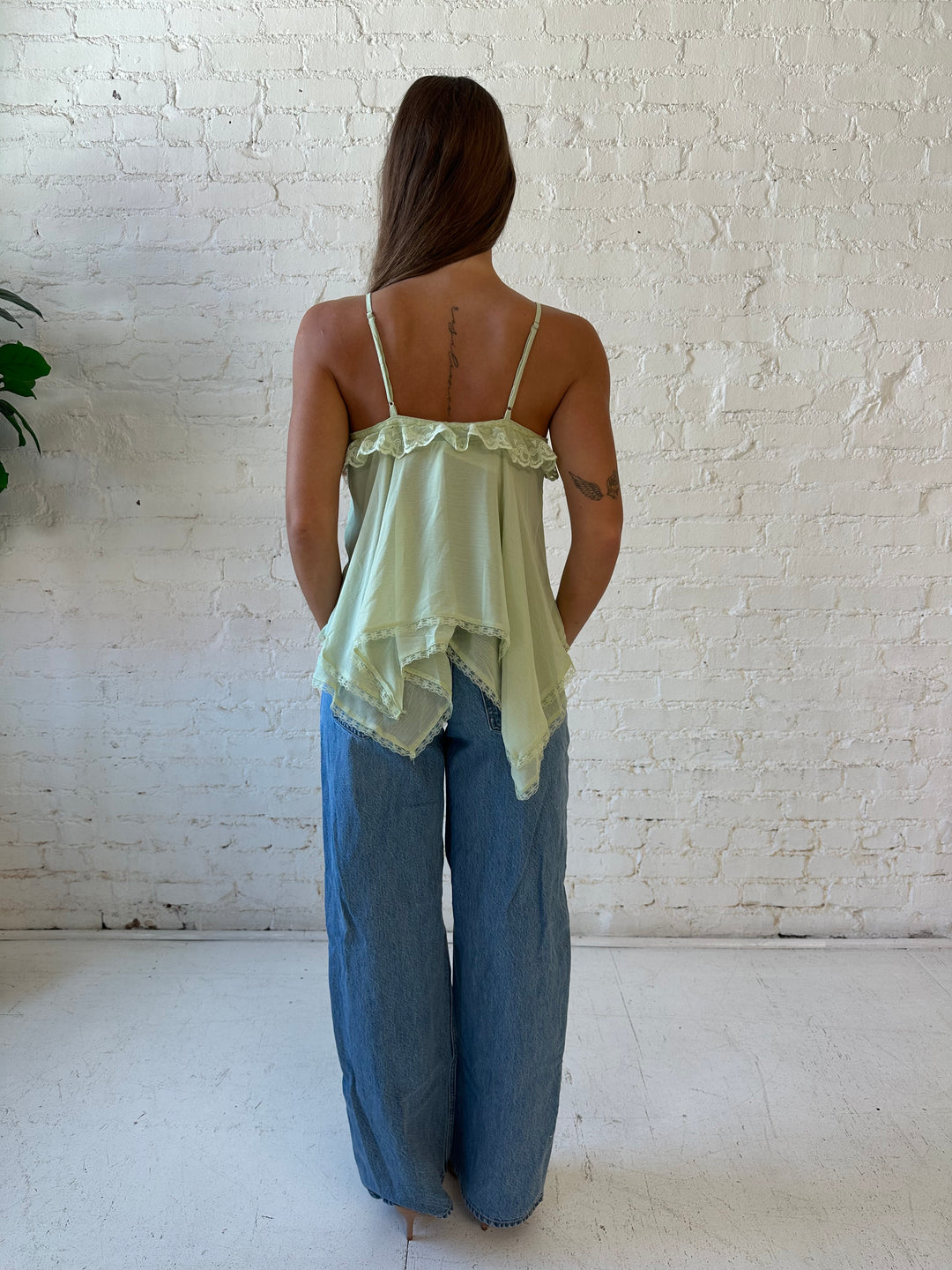 Woman wearing sage green flouncy tiered top with medium wash jeans. 
