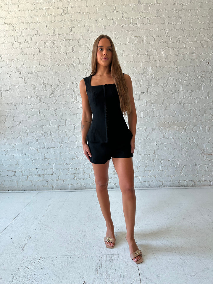 Woman wearing black tailored two piece set with front clasp closure.