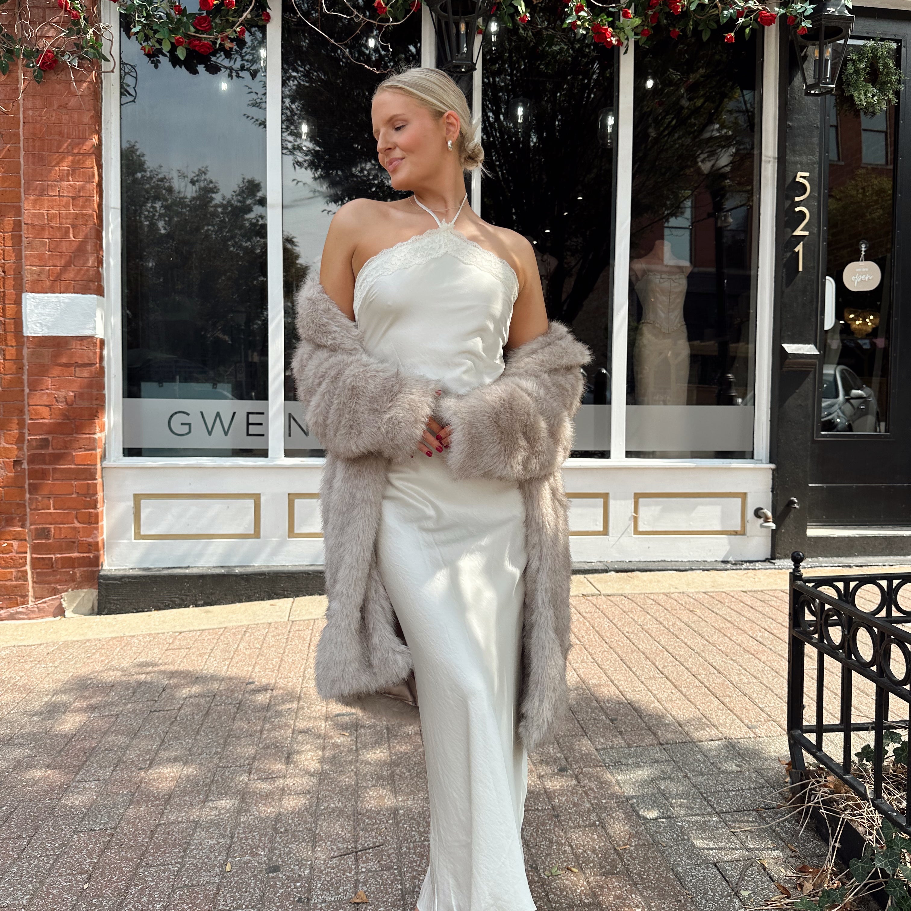 Woman wearing beige faux fur coat over white satin slip dress.