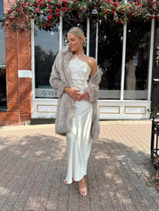 Woman wearing beige faux fur coat over white satin slip dress.