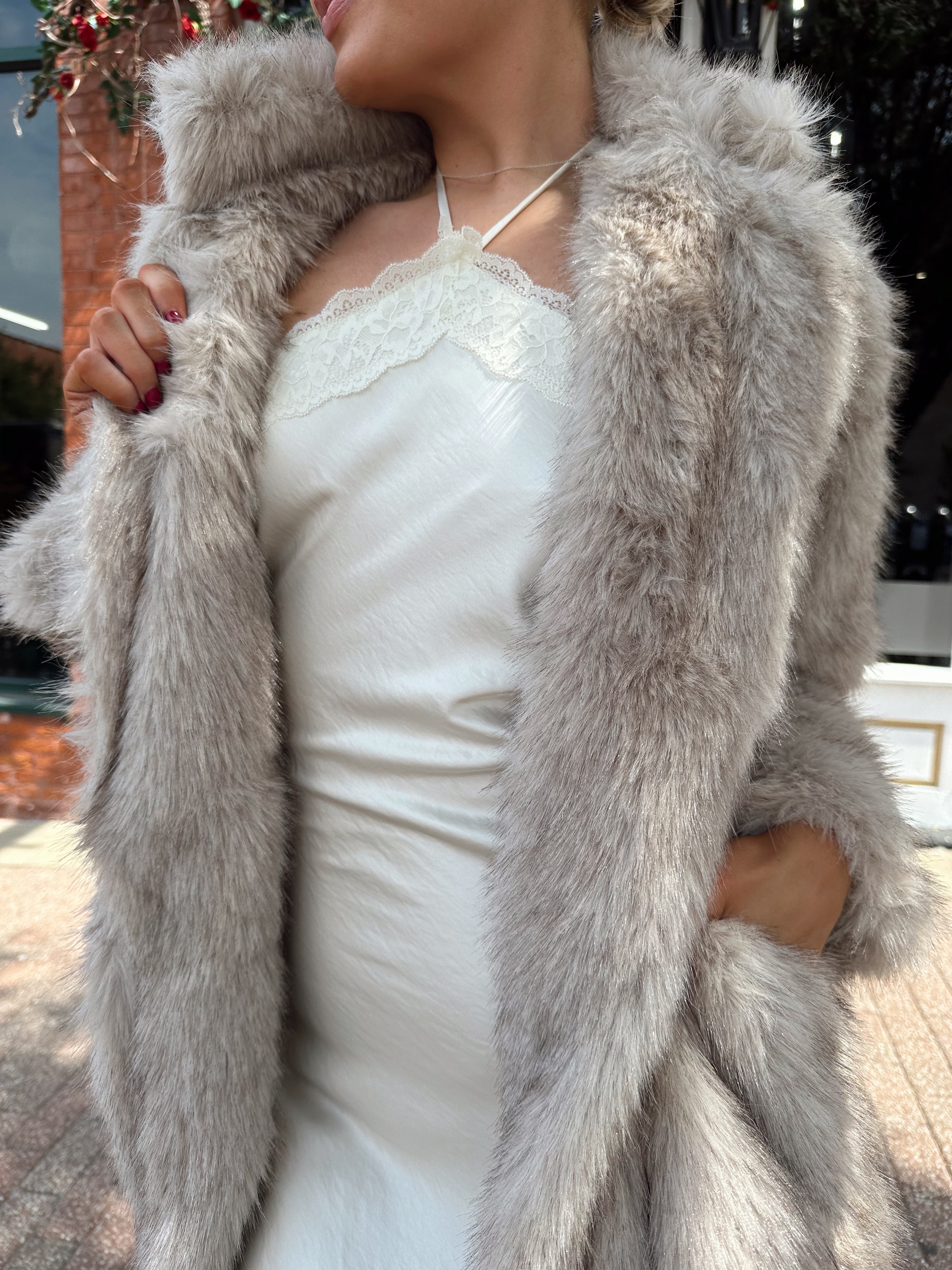 Woman wearing beige faux fur coat over white satin slip dress.