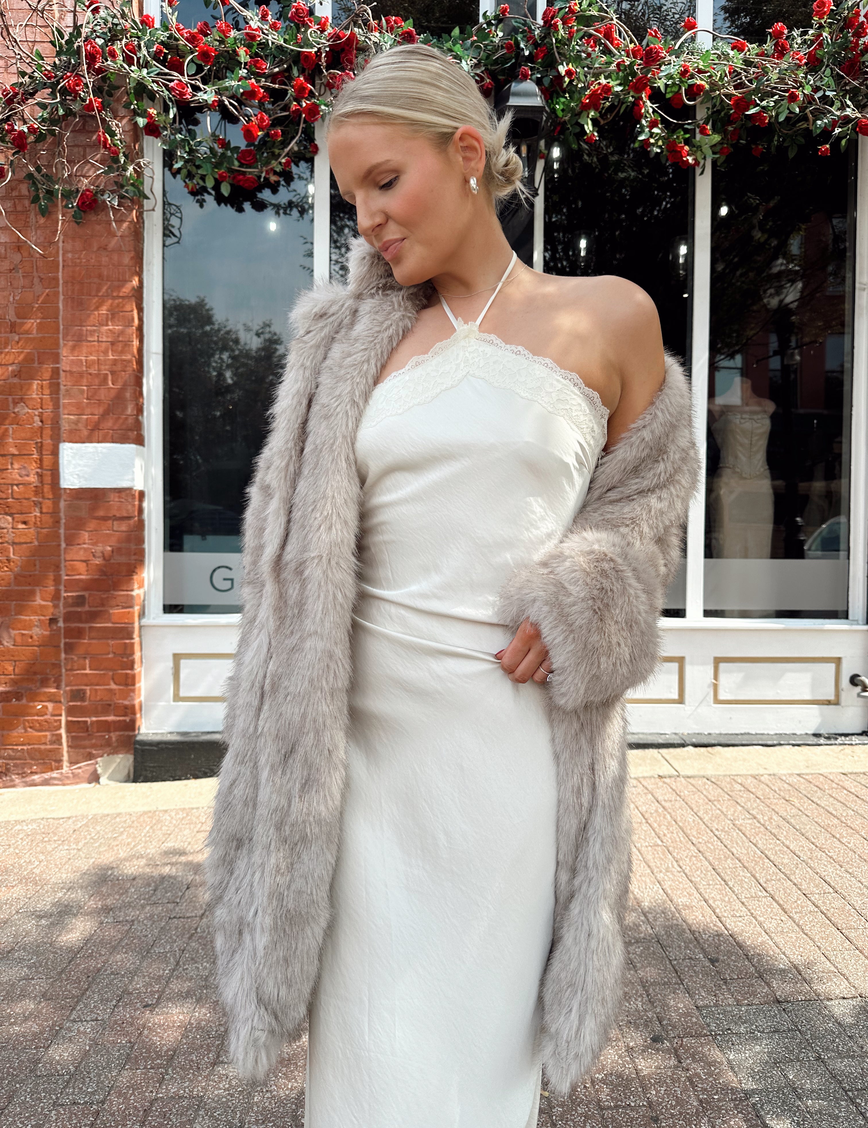 Woman wearing beige faux fur coat over white satin slip dress.