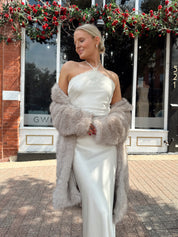 Woman wearing beige faux fur coat over white satin slip dress.
