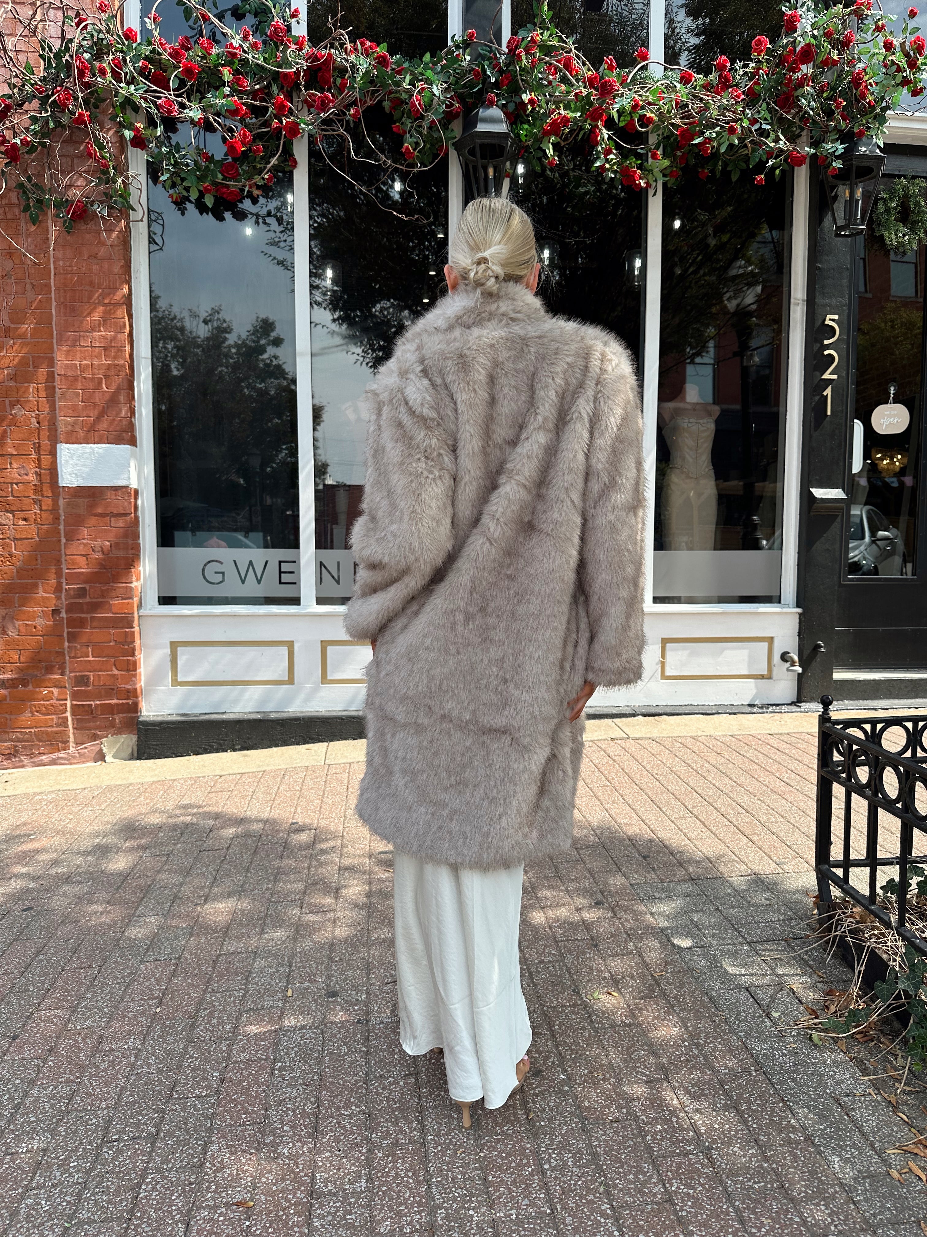 Woman wearing beige faux fur coat over white satin slip dress.