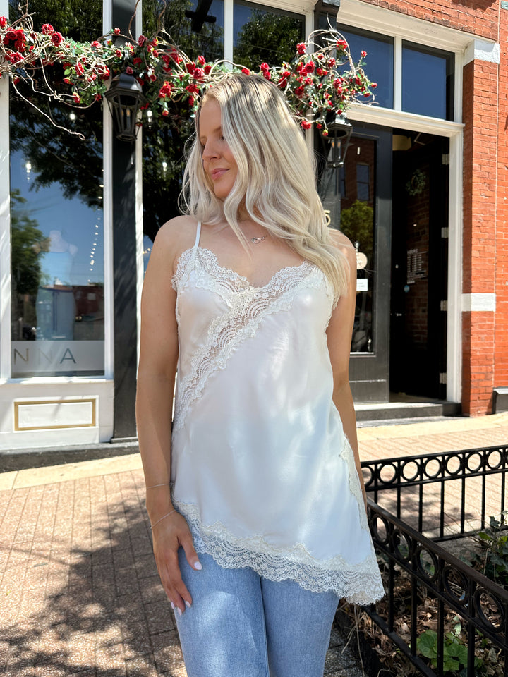 Woman wearing cream lace trim asymmetrical tank top with distressed jean. 