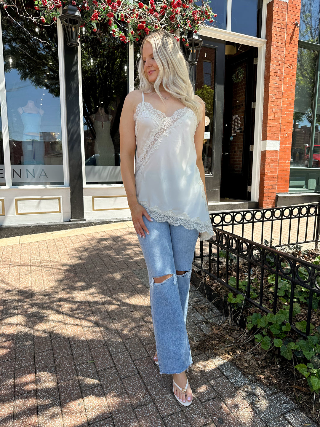Woman wearing cream lace trim asymmetrical tank top with distressed jean. 