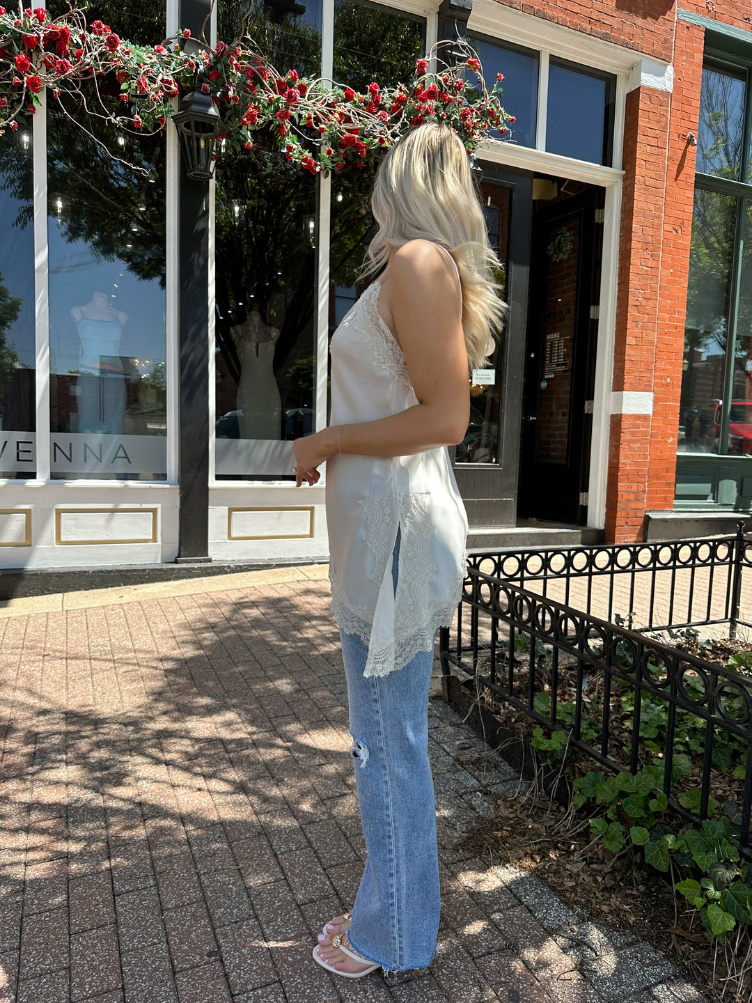 Woman wearing cream lace trim asymmetrical tank top with distressed jean. 