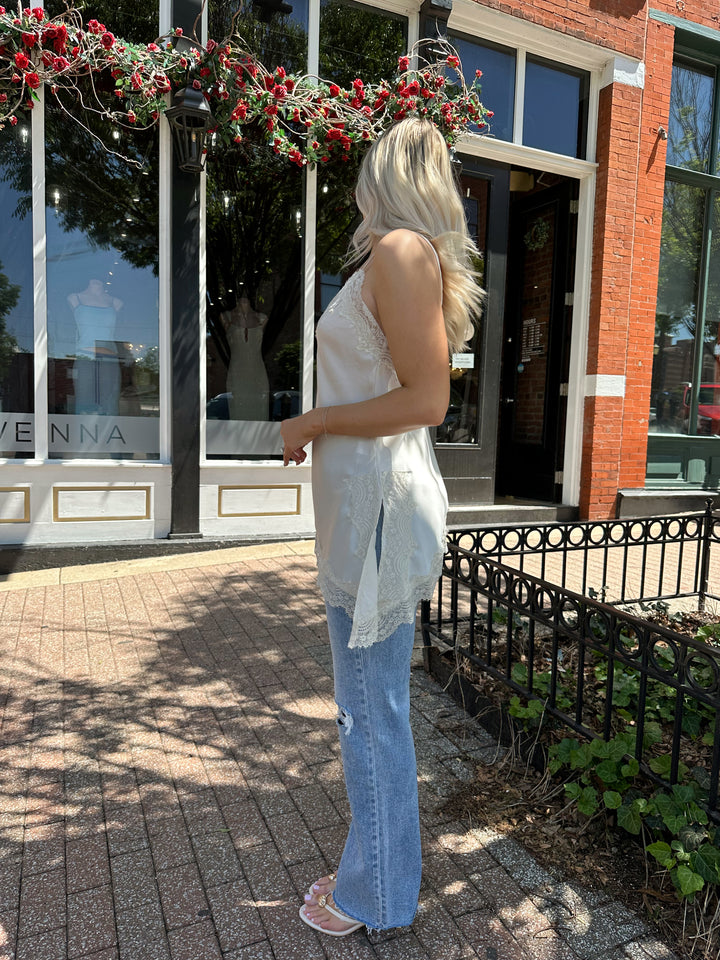 Woman wearing cream lace trim asymmetrical tank top with distressed jean. 
