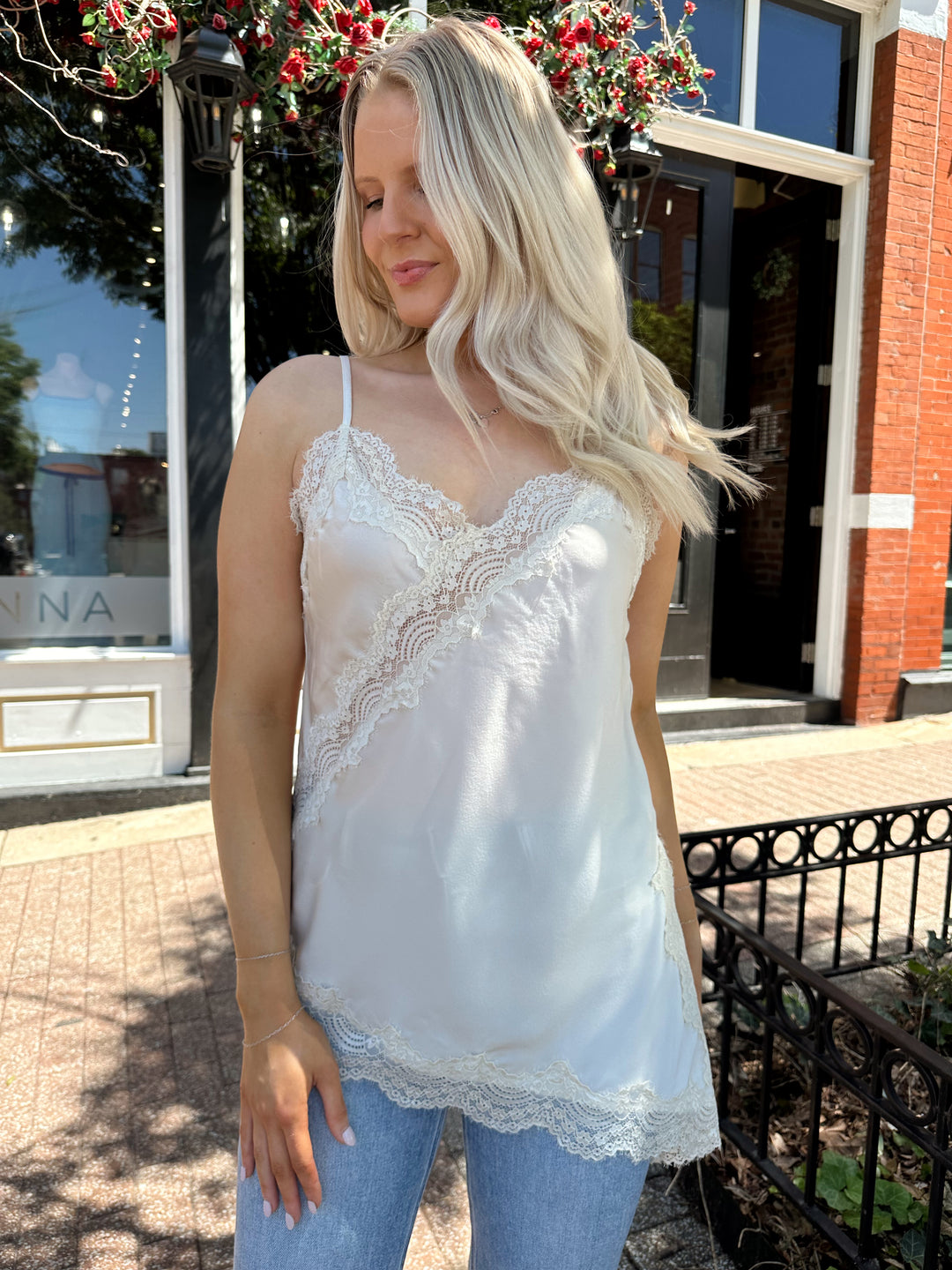 Woman wearing cream lace trim asymmetrical tank top with distressed jean. 