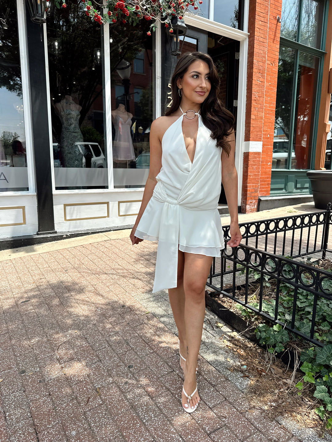 Woman wearing cream colored mini dress with self tie halter top and ring detail.