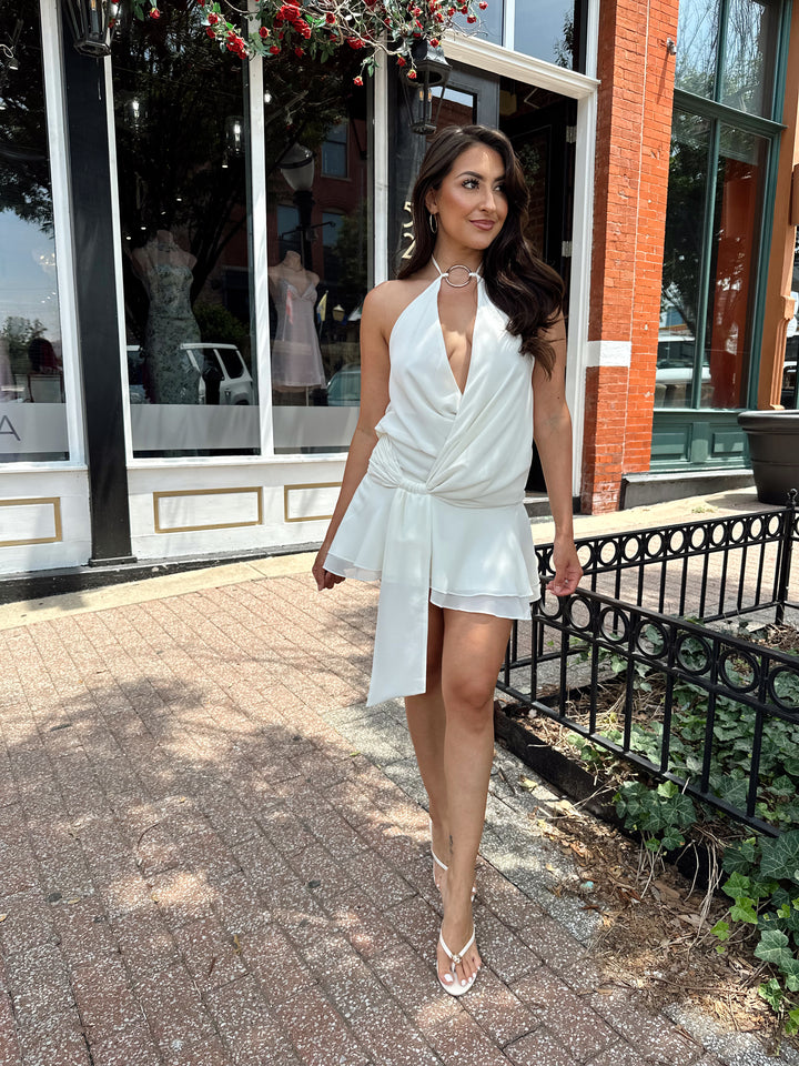 Woman wearing cream colored mini dress with self tie halter top and ring detail.
