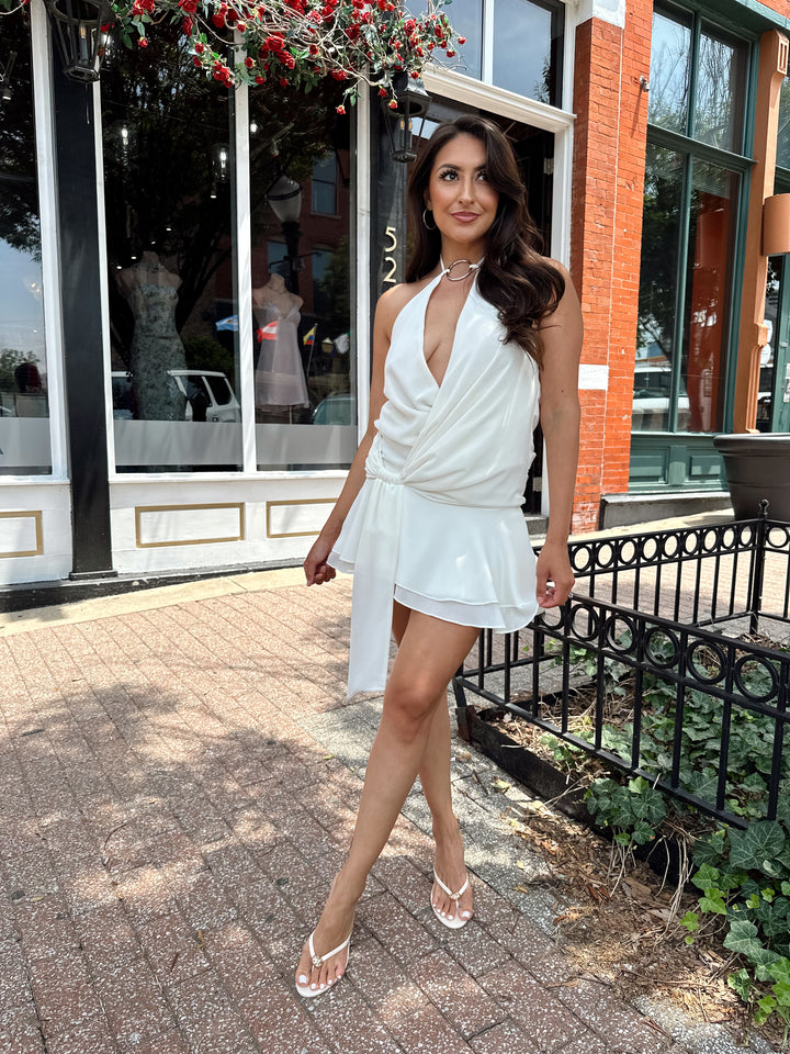 Woman wearing cream colored mini dress with self tie halter top and ring detail.