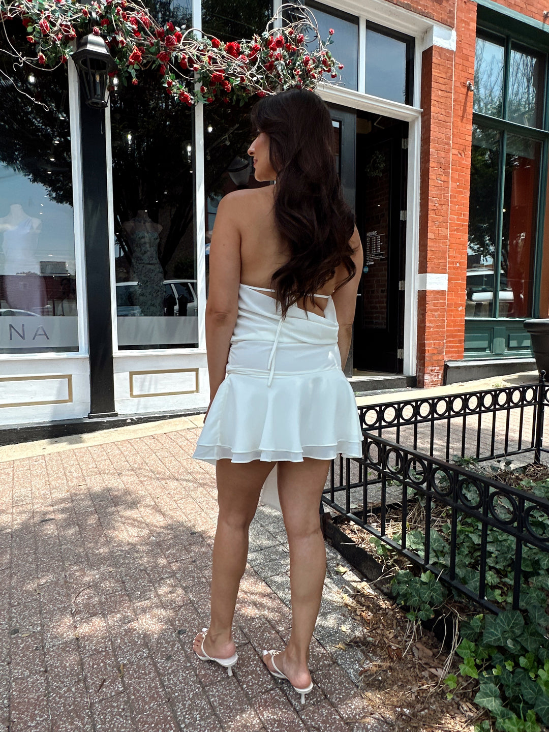 Woman wearing cream colored mini dress with self tie halter top and ring detail.