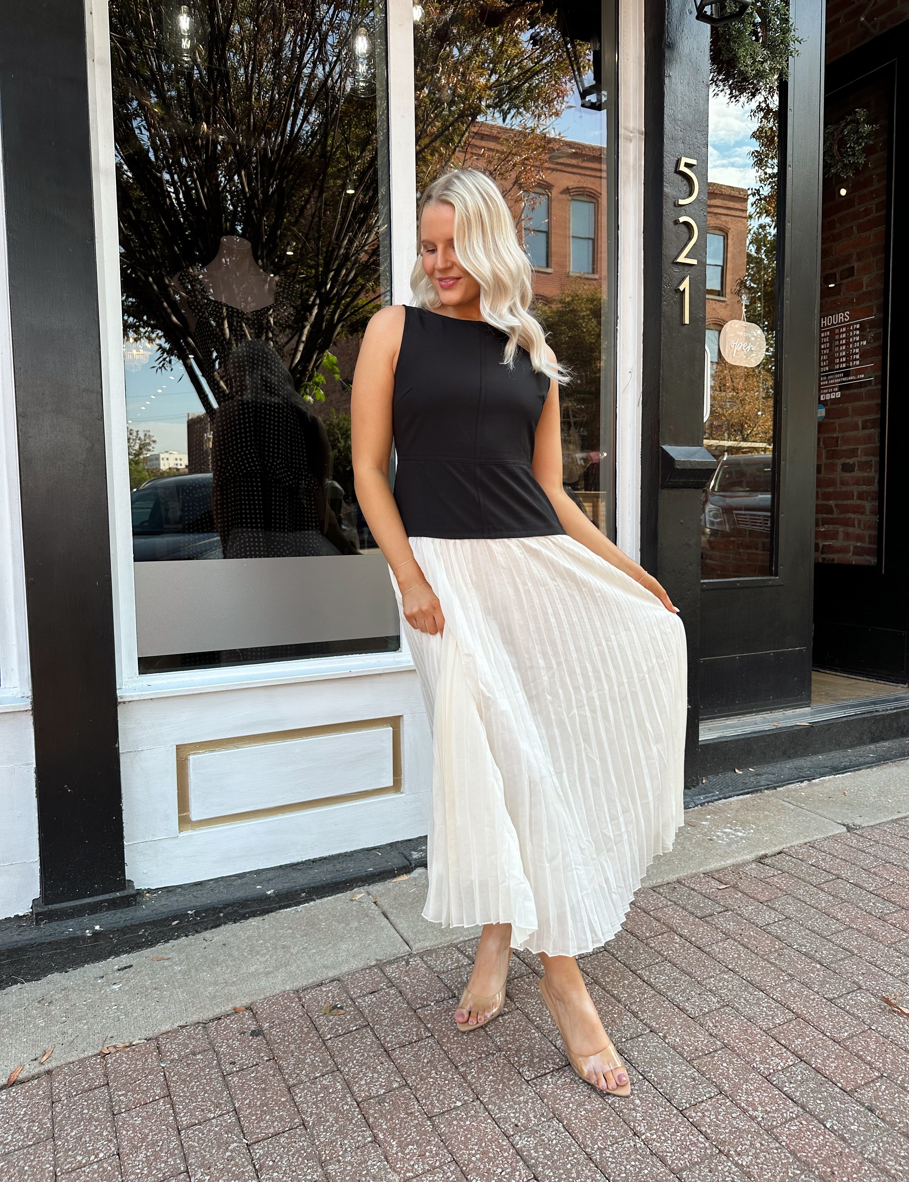 Woman wearing contrast midi dress with black top and cream pleated skirt. 