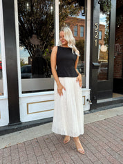 Woman wearing contrast midi dress with black top and cream pleated skirt. 