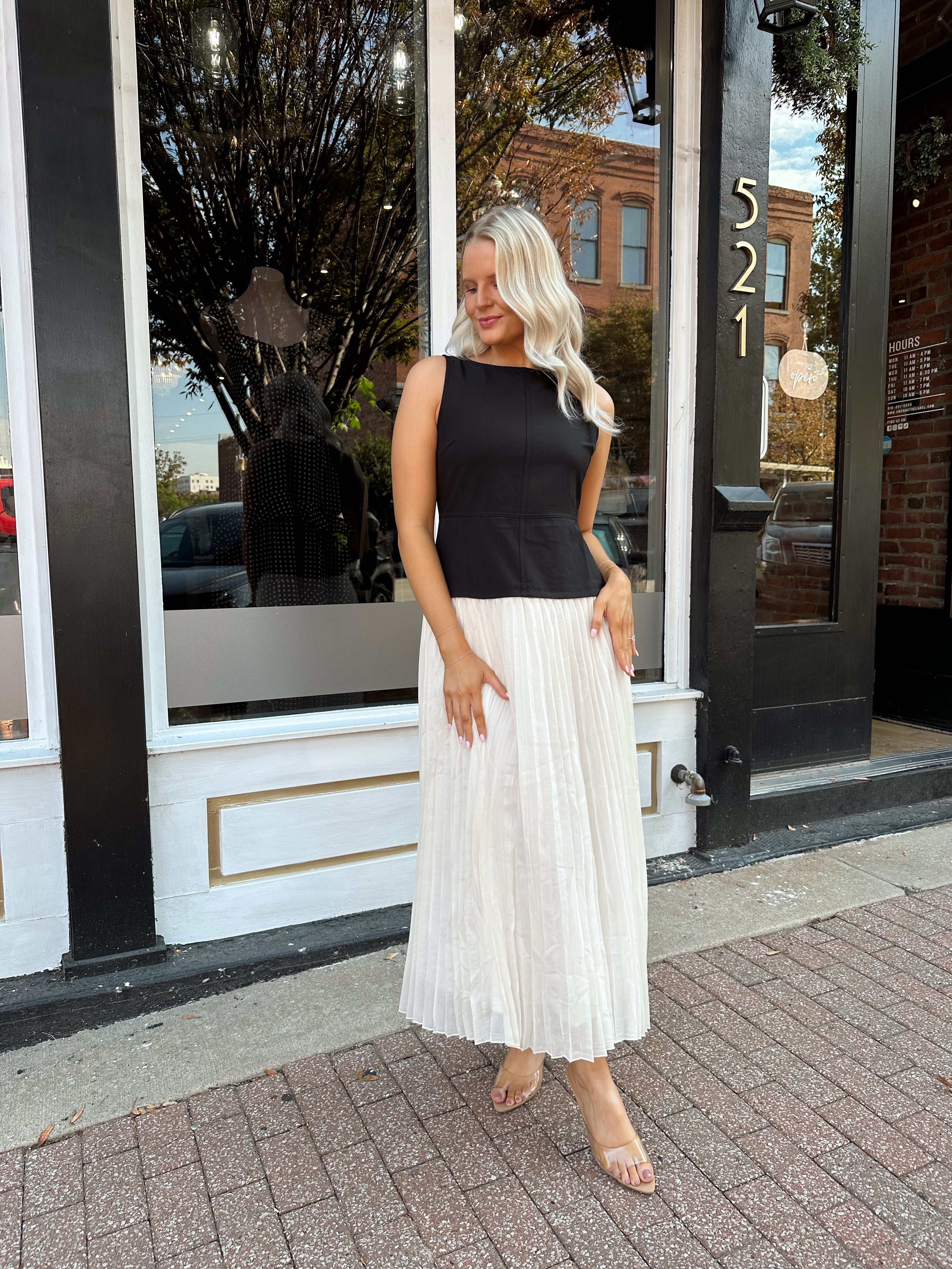 Woman wearing contrast midi dress with black top and cream pleated skirt. 