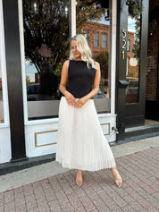 Woman wearing contrast midi dress with black top and cream pleated skirt. 
