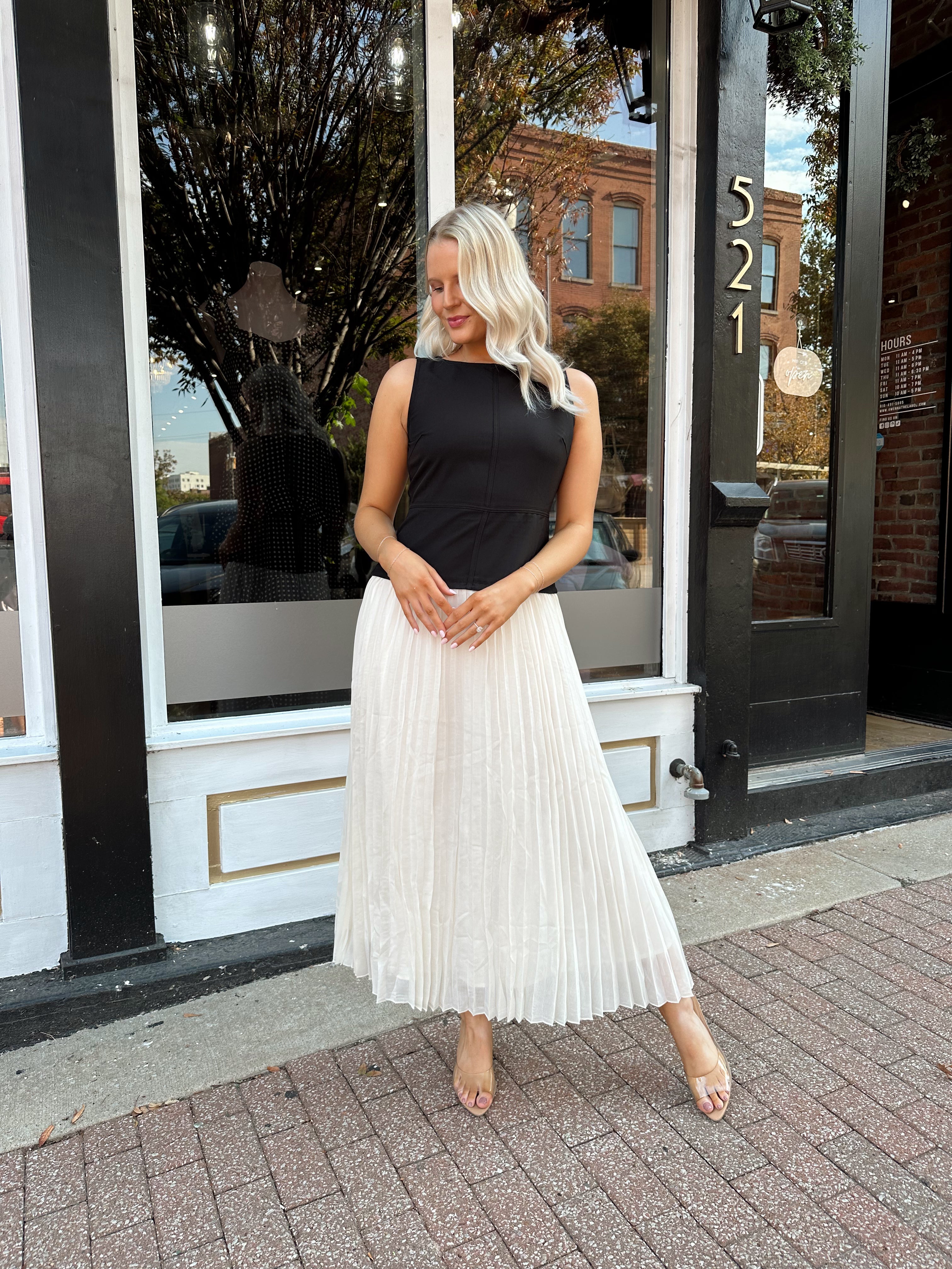 Woman wearing contrast midi dress with black top and cream pleated skirt. 