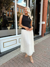 Woman wearing contrast midi dress with black top and cream pleated skirt. 